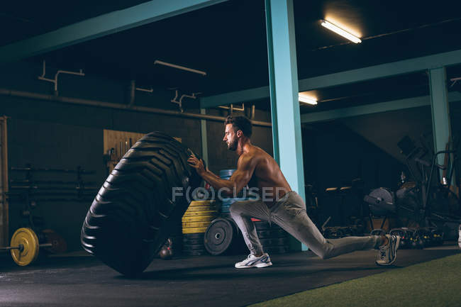 Homem musculoso exercitando com pneu pesado no estúdio de fitness — Fotografia de Stock