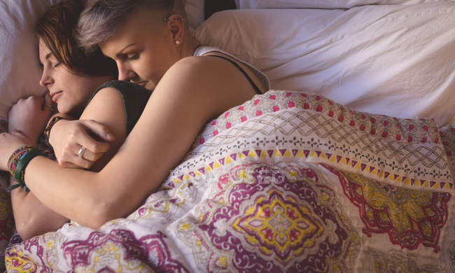 Casal de lésbicas abraçando enquanto dorme na cama no quarto em casa . — Fotografia de Stock