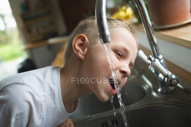Primo piano del ragazzo che beve acqua dal rubinetto in cucina a casa — Foto stock