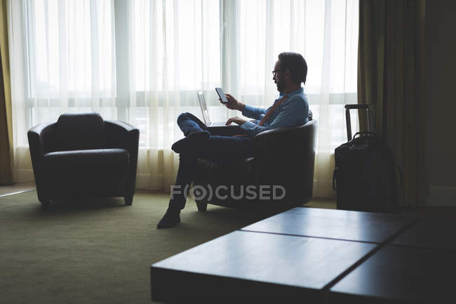 Бизнесмен, использующий цифровой планшет и ноутбук в номере отеля — стоковое фото
