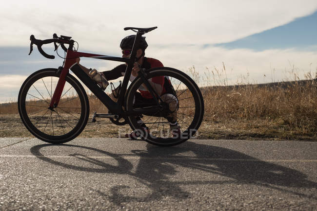 Biker kontrolliert an sonnigem Tag sein Mountainbike auf der Straße — Stockfoto