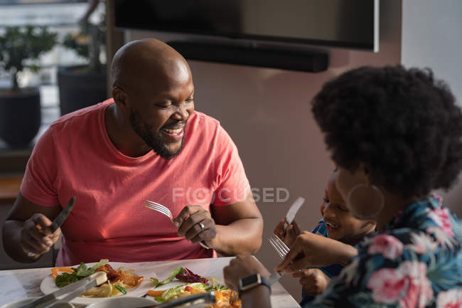 Family with son laughing while eating at dinning table at home. — Stock Photo