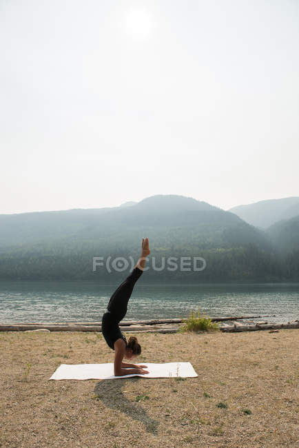 Mujer en forma haciendo yoga acrobático cerca de la costa del mar en un día soleado - foto de stock