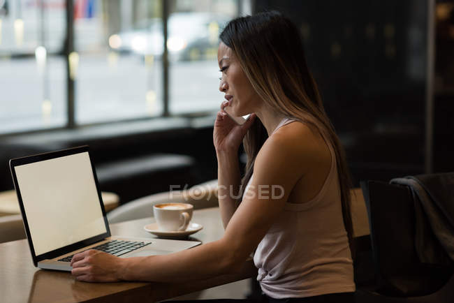 Businesswoman talking on phone while working on laptop in the cafeteria — Stock Photo