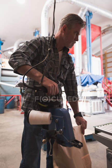 Man packing refined grains with machine in factory — Stock Photo
