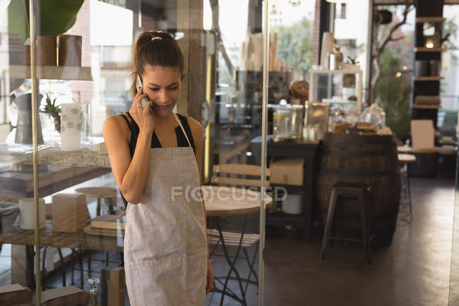 Camarera sonriente hablando por teléfono móvil en la cafetería - foto de stock
