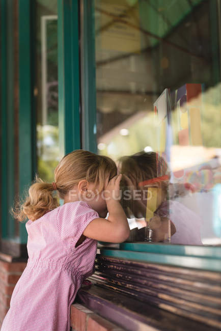 Chica espiando a través de la ventana de cristal fuera de la librería - foto de stock
