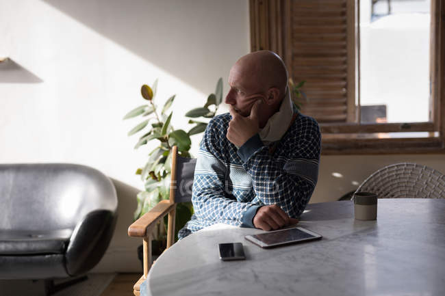 Nachdenklicher Mann sitzt auf Stuhl am Tisch mit digitalem Tablet im heimischen Wohnzimmer. — Stockfoto