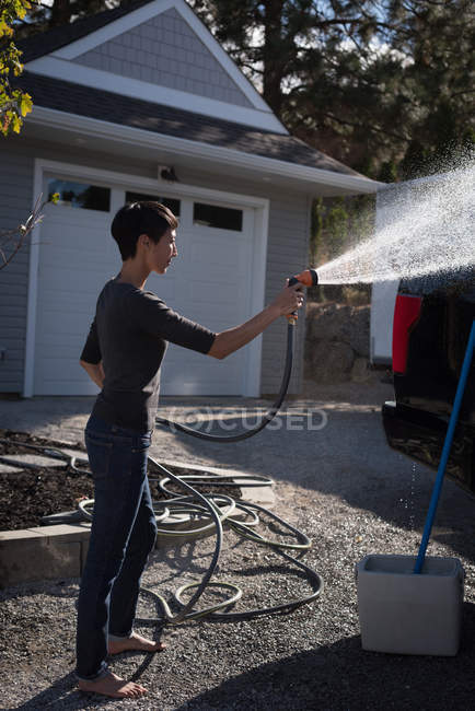 Vista lateral de la mujer lavando su coche con un chorro de agua de alta presión - foto de stock