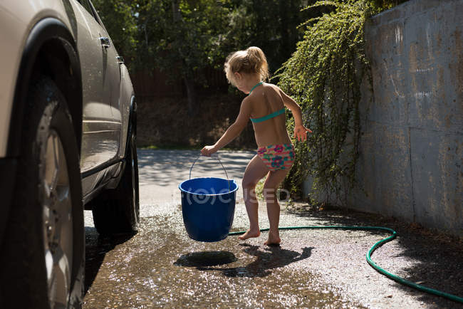 Chica sosteniendo cubo azul mientras se lava el coche - foto de stock