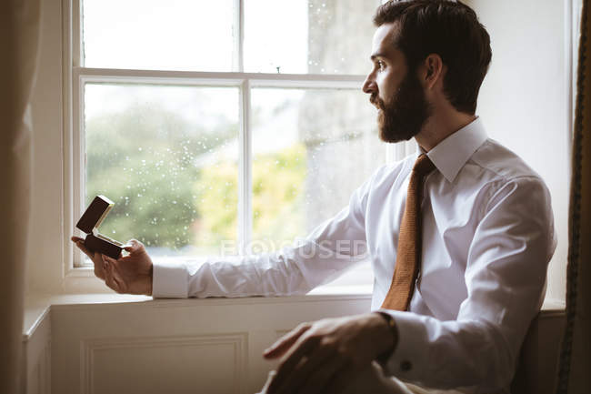 Задумчивый жених сидит с кольцом коробка возле окна — стоковое фото