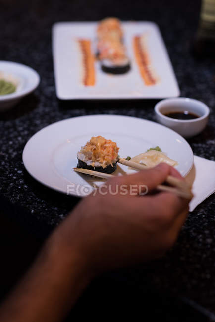 Un homme ramasse des sushis avec des baguettes dans un restaurant — Photo de stock