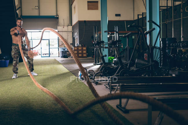 Решительный мускулистый мужчина тренируется с веревкой в фитнес-студии — стоковое фото