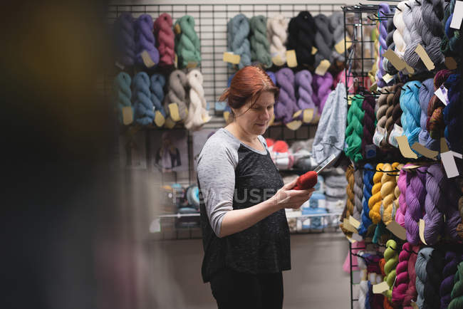 Жінка дивиться на пряжу під час використання цифрового планшета в кравецькому магазині — стокове фото