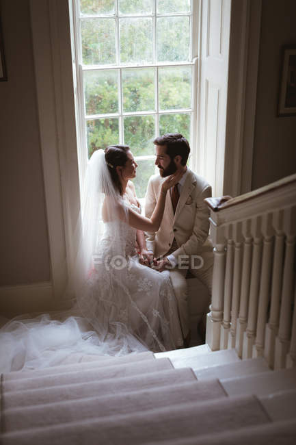 Romantic bride and groom sitting on the window sill at home — Stock Photo