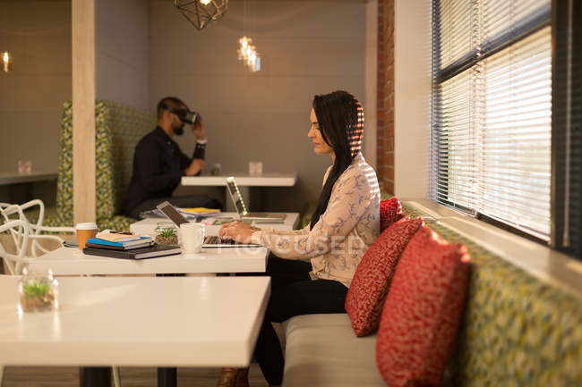 Femme exécutive utilisant un ordinateur portable à la cafétéria au bureau — Photo de stock