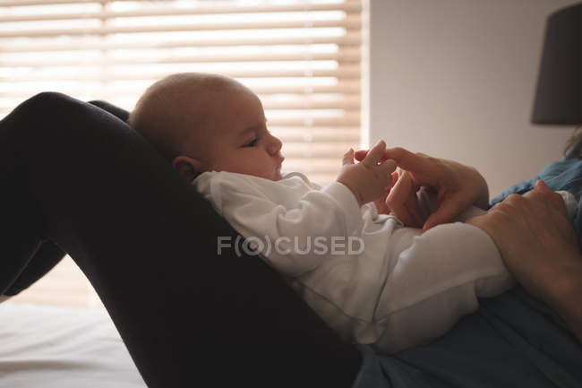 Junge Mutter sitzt im Bett, hält Baby auf dem Schoß und spielt zu Hause — Stockfoto