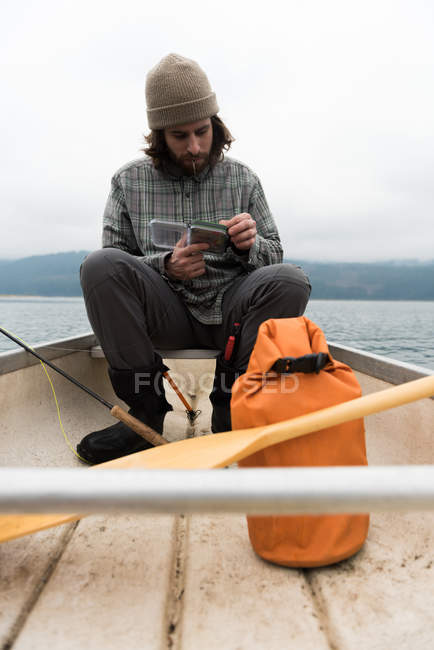 Homem escolhendo isca de caixa de isca enquanto sentado em barco — Fotografia de Stock