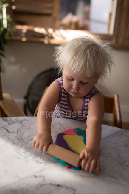 Toddler girl rolling up clay in living room at home. — Stock Photo