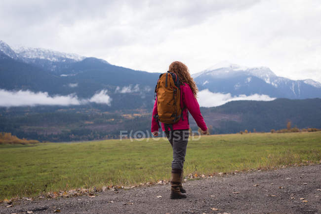 Вид ззаду жінки, що йде на ґрунтовій доріжці проти снігового покриву гори і пейзажу — стокове фото