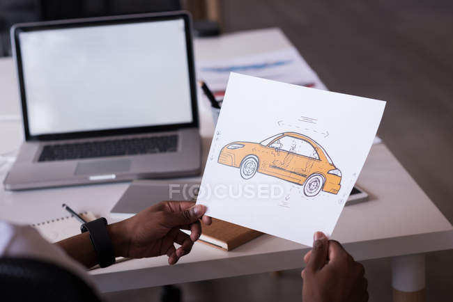 Hombre con un dibujo de coche sentado en el escritorio con el ordenador portátil - foto de stock