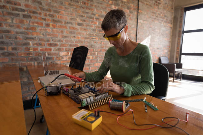 Ingeniera eléctrica femenina placa de circuito de soldadura en la oficina . - foto de stock