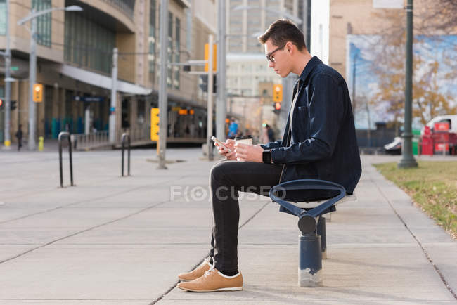 Чоловік використовує мобільний телефон, маючи каву на вулиці — стокове фото