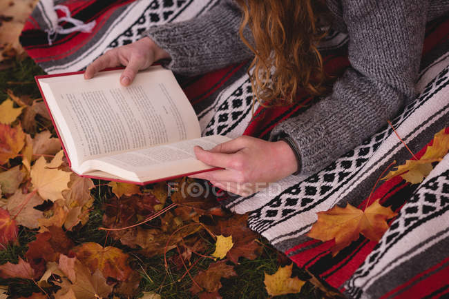 Крупный план женщины, лежащей в осеннем парке и читающей книгу — стоковое фото