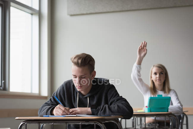 Teenage girl raising hand in classroom at university — Stock Photo