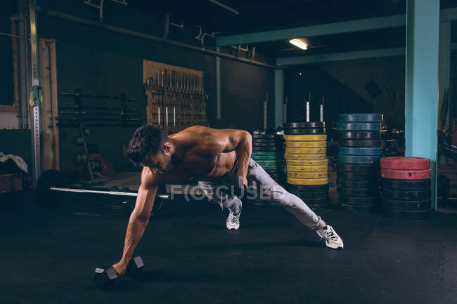 Muscular man doing push-up with dumbbells in fitness studio — Stock Photo
