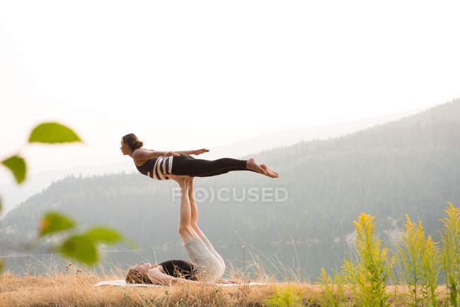 Спортивная пара, практикующая акро-йогу на пышной зеленой земле во времена Двана — стоковое фото