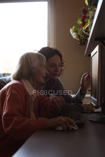 Cuidador que ayuda a la mujer mayor mientras trabaja en la computadora en la sala de enfermería - foto de stock