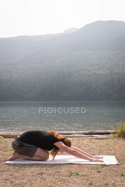Vista lateral del hombre en forma haciendo yoga acrobático cerca de la costa del mar - foto de stock