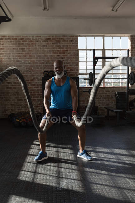 Determined senior man doing cross fit rope training in fitness studio. — Stock Photo