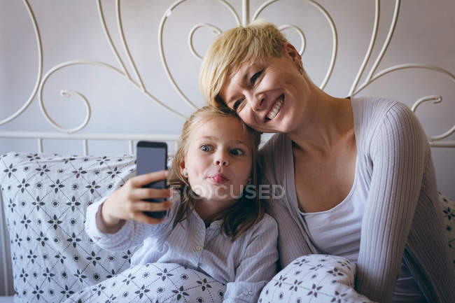 Madre e hija tomando selfie con teléfono móvil en casa - foto de stock