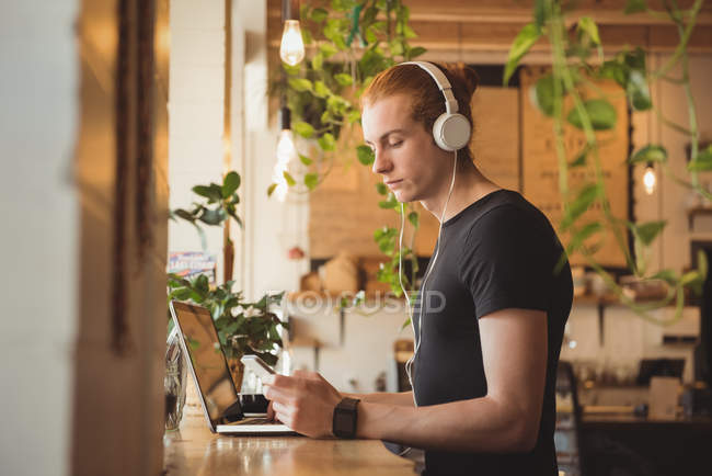 Человек слушает музыку на наушниках, а мобильный телефон в кафе — стоковое фото