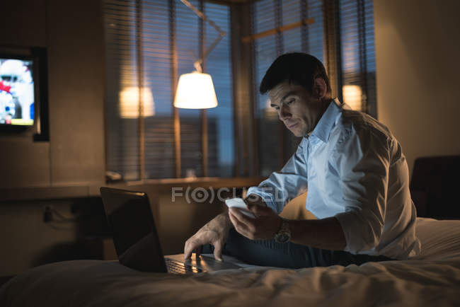Empresario con portátil y teléfono móvil en el dormitorio del hotel - foto de stock