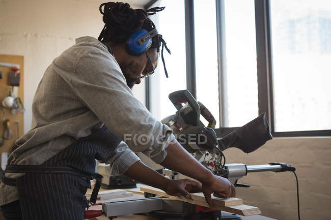 Charpentier découpe planche de bois avec scie électrique en atelier — Photo de stock