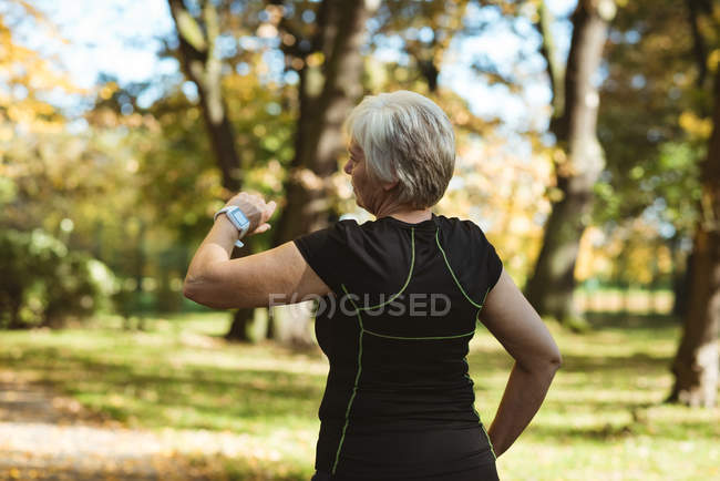 Старша жінка, використовуючи розумний годинник в парку в сонячний день — стокове фото