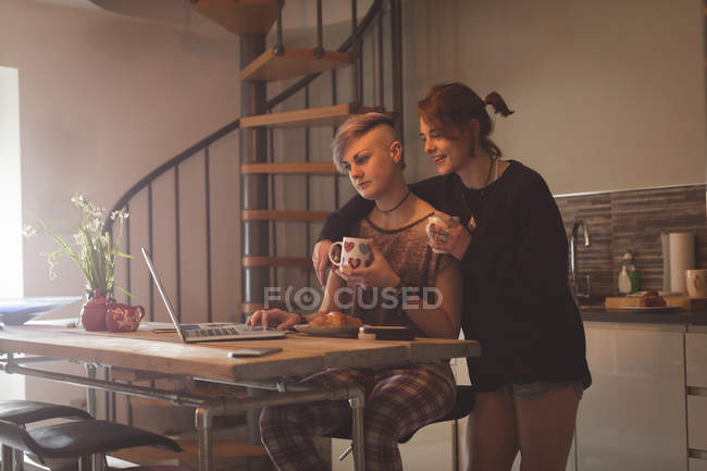 Pareja lesbiana usando portátil mientras toma café en casa . - foto de stock