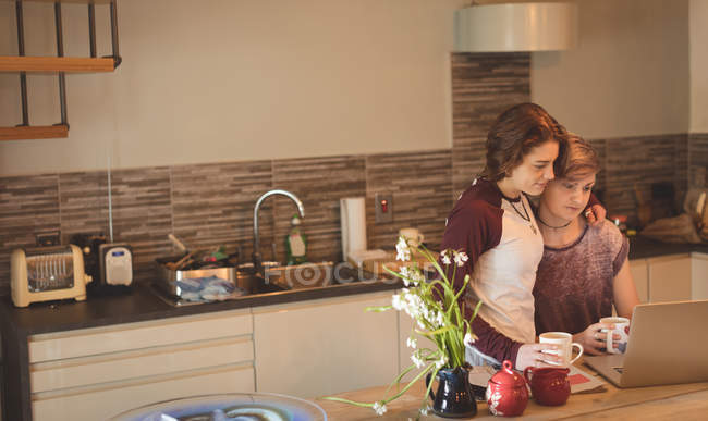Couple lesbien utilisant un ordinateur portable tout en prenant un café à la cuisine . — Photo de stock