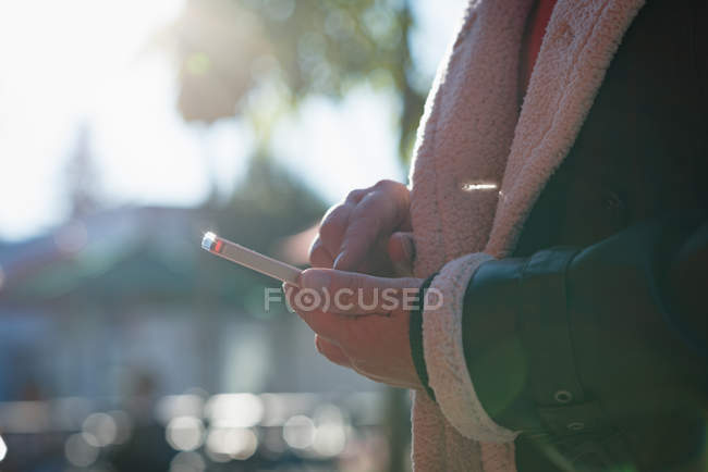 Средняя секция женщины, использующей мобильный телефон в солнечный день — стоковое фото