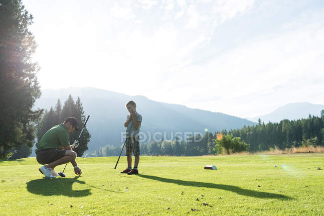 Отец регулирует мяч для гольфа на Ти в поле — стоковое фото