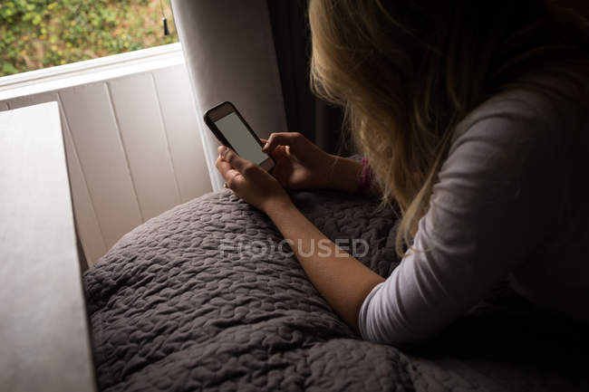 Jovem mulher usando seu telefone celular deitado na cama no quarto — Fotografia de Stock