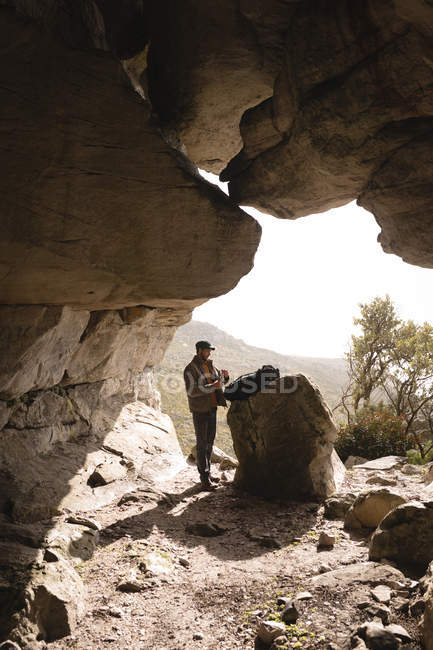 Турист, стоящий у входа в пещеру в солнечный день — стоковое фото
