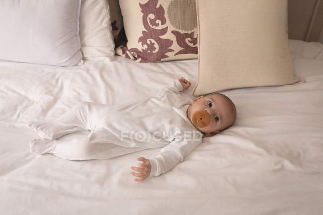 Niedliches kleines Baby mit Schnuller im Mund schläft zu Hause auf dem Bett — Stockfoto
