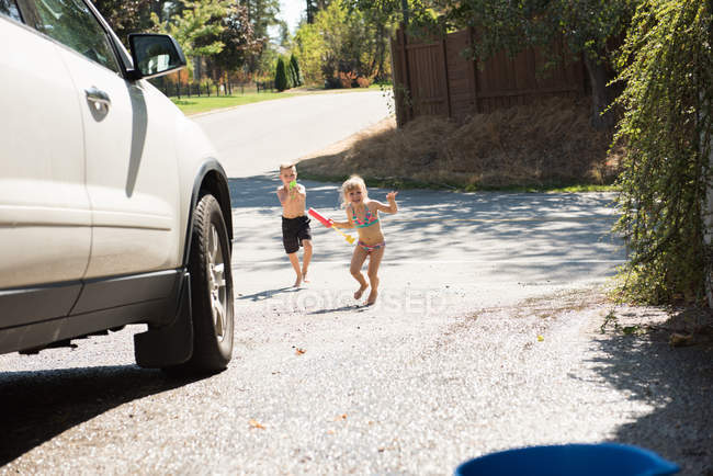 Siblings playing with water gun at outside garage — Stock Photo