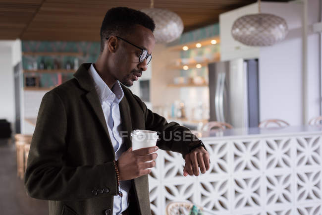Businessman looking at smartwatch while having coffee in cafeteria at creative office — Stock Photo