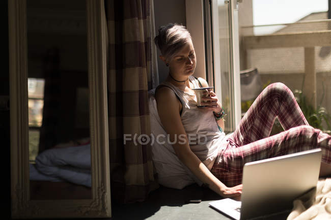 Femme utilisant un ordinateur portable tout en prenant un café à la maison
. — Photo de stock