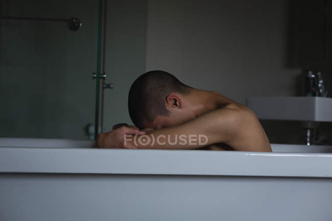 Jeune homme déprimé assis dans la baignoire à la salle de bain — Photo de stock